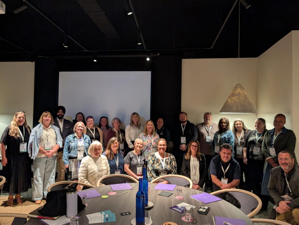 Group photo of homelessness sector professionals at a Homelessness Queensland event, seated and standing in a conference room.